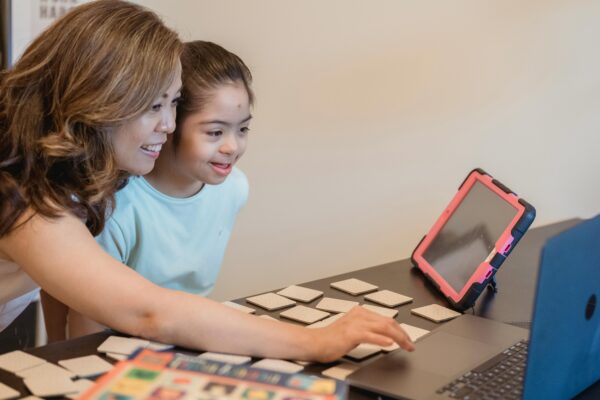 A teacher showing a student something on a laptop and tablet.